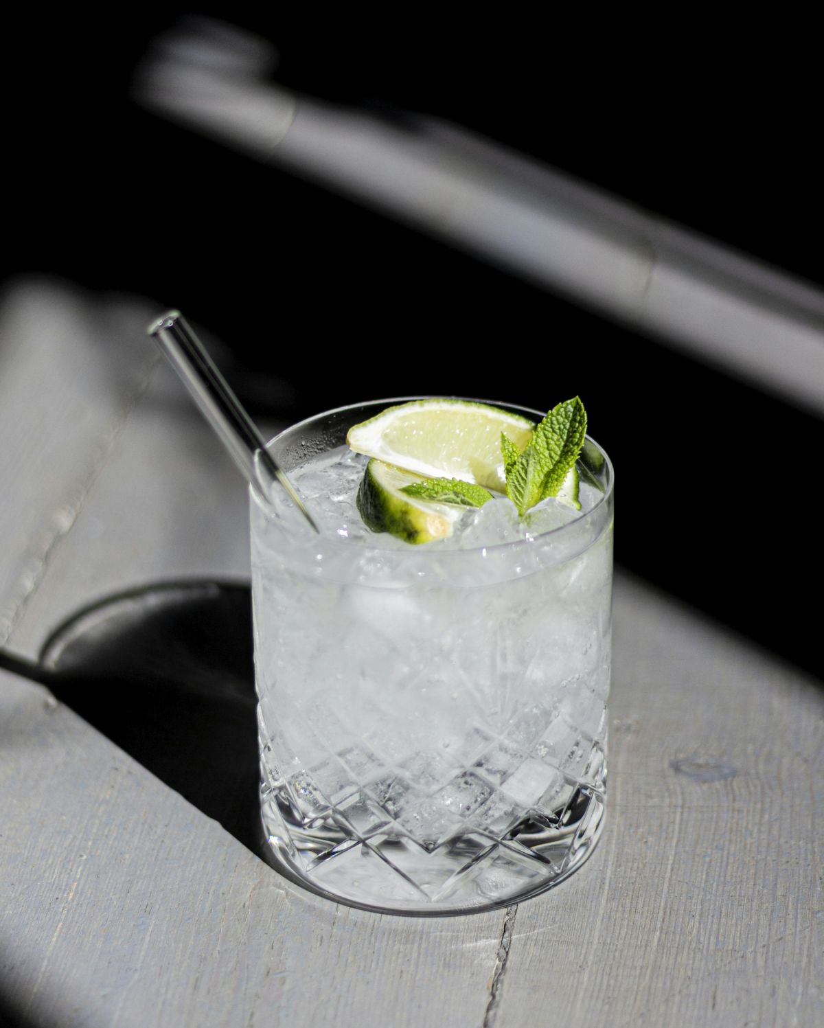 Crystal cut tumbler of ice with lime wedge and fresh mint in sunlight