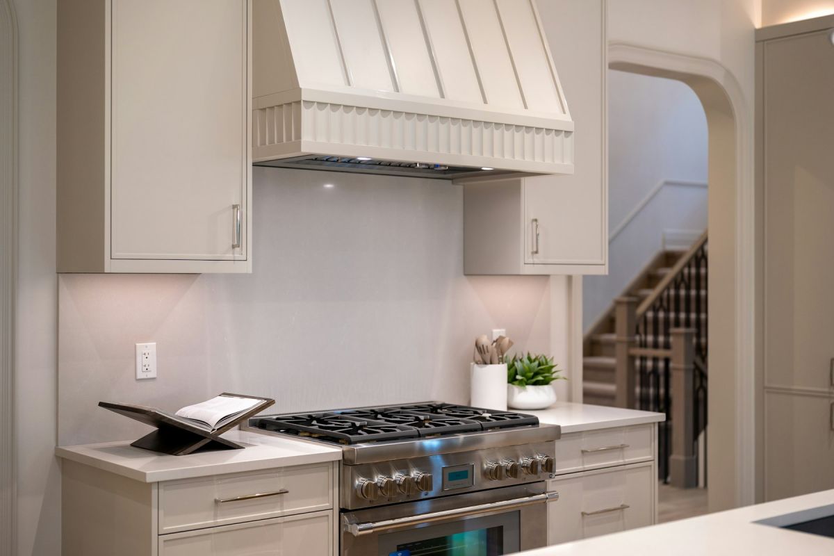 Sculptural cream range hood with banded detail above a stainless steel range with gas burners and cabinetry